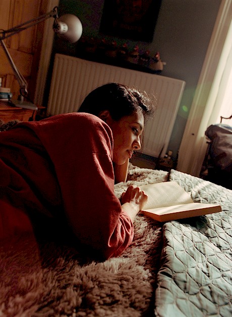 woman lying forward on bed reading book sun and shadows on her face shot by Meghan Eagles represented by Horton-Stephens photographers' agents
