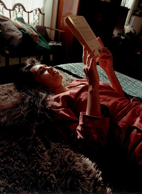 woman lying  back on bed reading book sun and shadows on her face shot by Meghan Eagles represented by Horton-Stephens photographers' agents