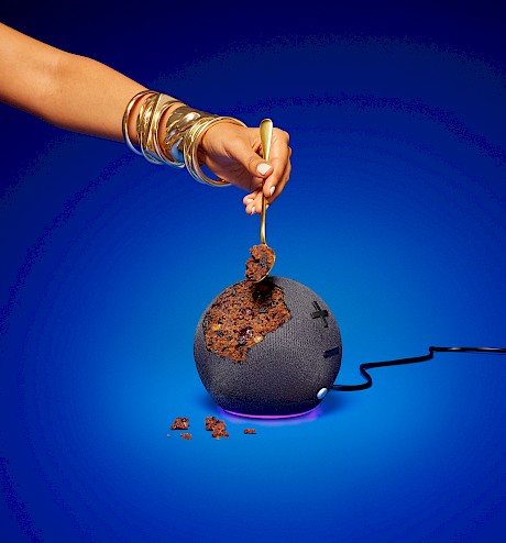 studio still life photograph of hand eating christmas pudding which is actually a blue tooth speaker photo by Wilson Henessy represented by Horton-Stephens photography agents